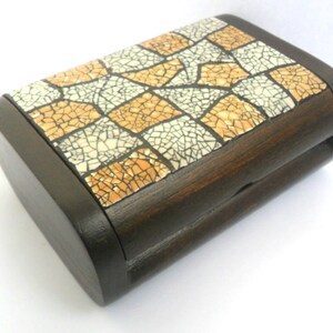 Puede incluir: Una caja de madera con tapa de mosaico. Las baldosas son una mezcla de beige y blanco con un acabado craquelado. La caja es de color marrón oscuro y tiene un borde redondeado.