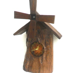 Könnte beinhalten: Eine Holzuhr in Form einer Windmühle mit einem braunen Zifferblatt und goldenen Zeigern. Die Uhr ist auf einem Stück Holz montiert, das wie ein Baumstamm aussieht.