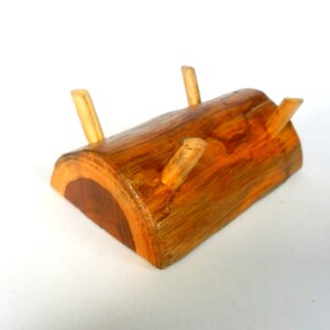 Puede incluir: Un soporte de madera en forma de tronco con tres clavijas de madera para sujetar objetos. El soporte est&aacute; hecho de madera natural de color marr&oacute;n y naranja.