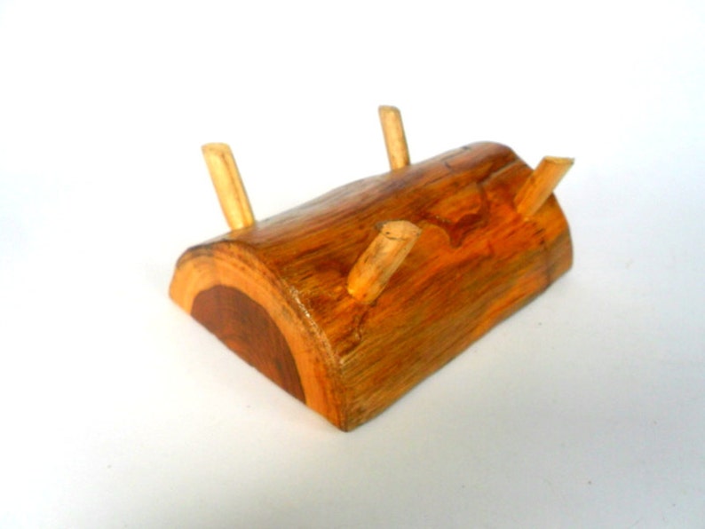 Puede incluir: Un soporte de madera en forma de tronco con tres clavijas de madera para sujetar objetos. El soporte est&aacute; hecho de madera natural de color marr&oacute;n y naranja.