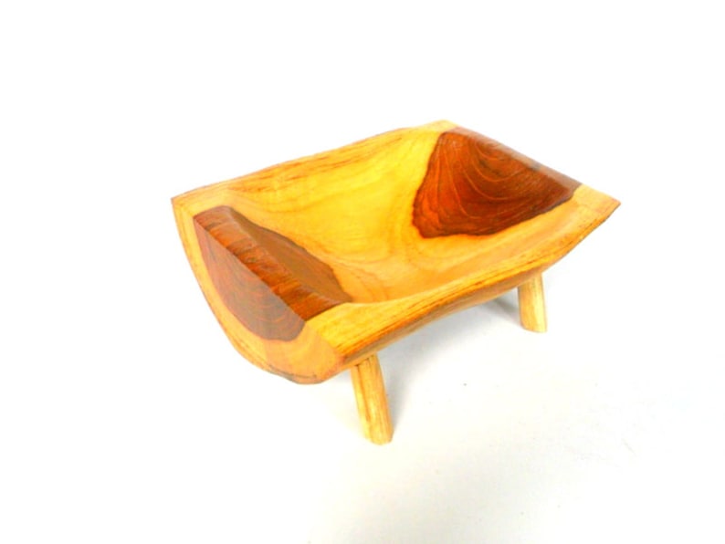 Puede incluir: Un cuenco de madera con un acabado de madera natural y un acento de madera marr&oacute;n oscuro. El cuenco est&aacute; sobre tres patas cortas.