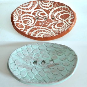 May include: Two ceramic soap dishes. One is a light brown color with a white swirl pattern. The other is a light blue color with a textured pattern.