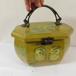 May include: A vintage wooden box purse with a brass handle and a hinged lid. The box is painted a muted green color and features a design of two owls and leaves.