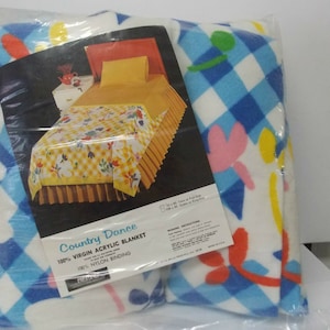 May include: A white and blue checkered blanket with a floral pattern. The blanket is packaged in plastic and has a label that reads "Country Dance 100% Virgin Acrylic Blanket 100% Nylon Binding".