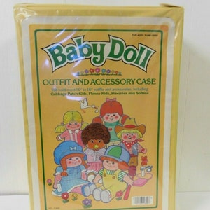 May include: Yellow cardboard box with a picture of a variety of baby dolls and the text "Baby Doll Outfit and Accessory Case" and "Will hold most 16" to 18" outfits and accessories, including Cabbage Patch Kids, Flower Kids, Preemies and Softina".