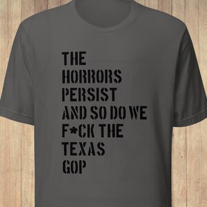 May include: A charcoal gray short-sleeved t-shirt featuring black stencil-style text that reads: THE HORRORS PERSIST AND SO DO WE F*CK THE TEXAS GOP. The shirt has a crew neckline and a standard fit, with a small circular logo in the bottom left corner.