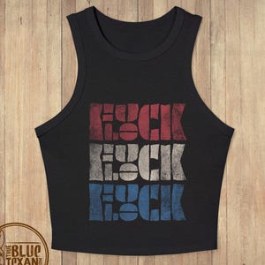 May include: A black sleeveless crop top featuring a distressed graphic print of the word "FLUCK" repeated three times in stacked rows. The top row is red, the middle row is white, and the bottom row is blue, creating a flag-like color scheme.