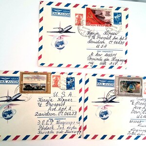 May include: Three vintage airmail envelopes with stamps and handwritten addresses. Each envelope features a stylized airplane and globe design, with red, white, and blue borders. The stamps depict landscapes and historical imagery.