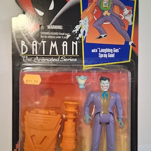 May include: The Joker action figure from Batman: The Animated Series. The figure is in a sealed package and includes a "Laughing Gas" spray gun. The Joker is wearing a purple suit, green vest, and blue bow tie. The packaging features Batman's silhouette.