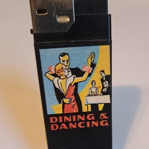 May include: A black lighter with a silver top. The lighter has a colorful image of a couple dancing with the text "DINING & DANCING" below.