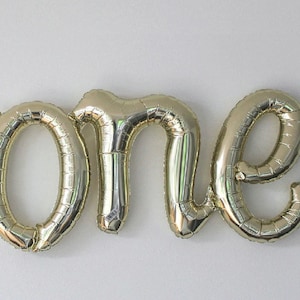 May include: Gold foil balloon letters spelling out the word "one".