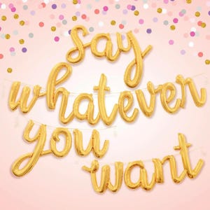 May include: Gold foil balloon letters spelling out "Say whatever you want" on a pink background with confetti.