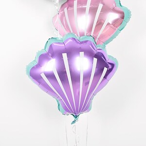 May include: Three iridescent foil balloons shaped like seashells. The balloons are pink, purple, and teal.