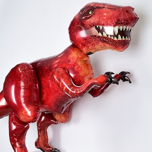 May include: A large red inflatable dinosaur balloon. The balloon is shaped like a Tyrannosaurus Rex with a detailed head and sharp teeth.