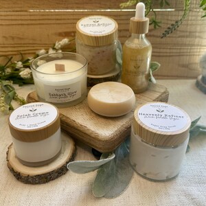 May include: A collection of self-care products, including a candle, body cream, sugar scrub, soap, and oil, arranged on wooden platforms. The products have white labels with text and wooden lids. The candle reads "Sabbath Glow Warm Vanilla Sugar."