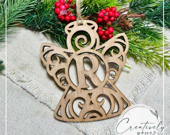 May include: Wooden angel ornament featuring a decorative swirl design with the letter "R" cut out in the centre. The ornament is unfinished and ready to be painted or stained.