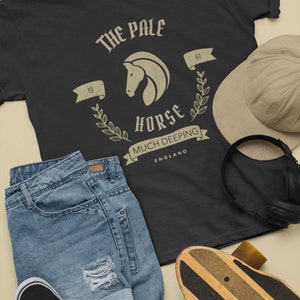 K&ouml;nnte beinhalten: Schwarzes T-Shirt mit einem Vintage-Grafikdruck eines Pferdekopfes mit dem Text "The Pale Horse" und "Much Deeping, England".