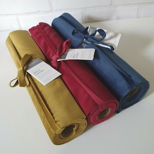 May include: Three fabric table runners rolled up, one mustard yellow, one red, and one blue. The yellow runner has a label that reads "VIVANT deco runner An 5354 10252 28 cm x 2.5 m".