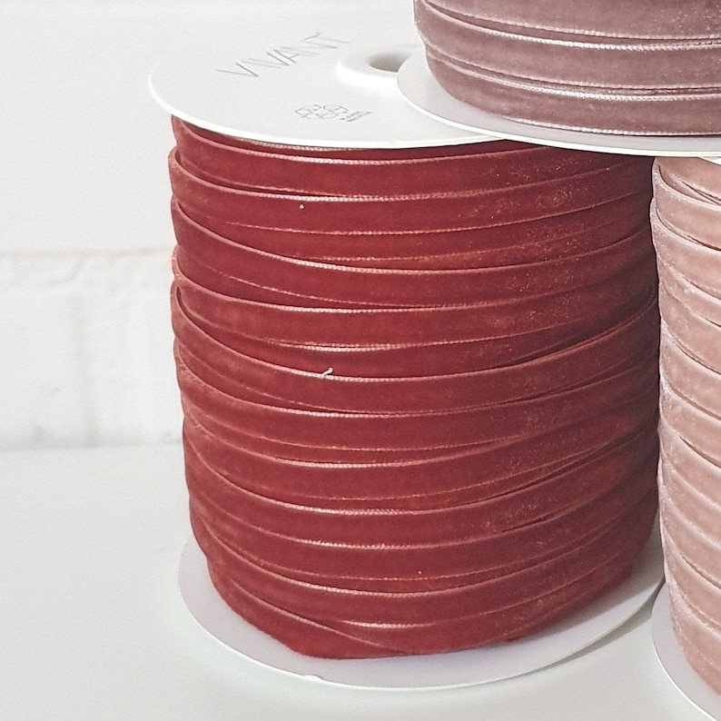 May include: A spool of rust-colored velvet ribbon. The ribbon is wound tightly around a white cardboard spool.