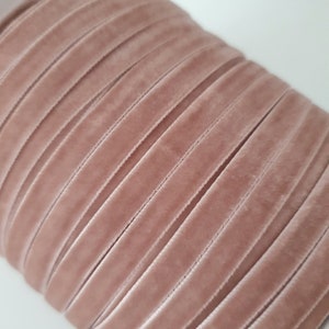 May include: A close-up of a spool of dusty rose velvet ribbon. The ribbon is arranged in neat rows, showcasing the soft, plush texture.