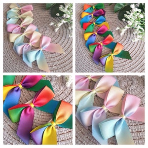 May include: Assortment of colourful ombre ribbon bows. The bows are made of satin ribbon and are tied in a classic bow shape. The colours of the bows include pink, blue, green, yellow, and purple.