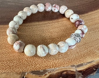 May include: A brown and white patterned stone bracelet with a silver bead accent. The bracelet is made of natural stones and is a great accessory for any outfit.