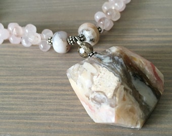 May include: A necklace with a large, faceted, pink and brown agate pendant. The necklace is made with small, pink rose quartz beads and silver spacers.