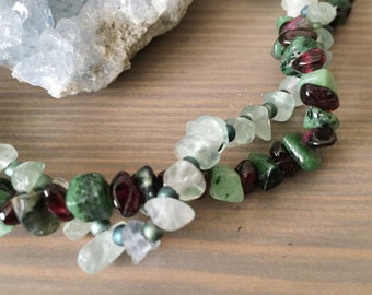 May include: A multi-strand necklace made with green, red, and white gemstone beads. The beads are irregularly shaped and appear to be natural stones.