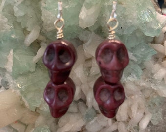 May include: A pair of dangle earrings featuring two stacked purple skull beads on silver ear wires.