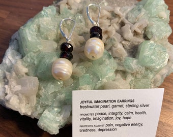 May include: Sterling silver earrings with a freshwater pearl and garnet beads. The earrings are designed to promote peace, integrity, calm, health, vitality, imagination, joy, and hope. They also protect against pain, negative energy, tiredness, and depression.  "JOYFUL IMAGINATION EARRINGS" and "WEARABLE HEALING ART" are printed on the card.