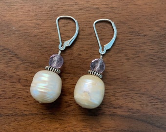 May include: A pair of silver earrings with a white pearl and a purple gemstone on each earring.