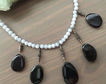 May include: A necklace made of light blue beads with five black teardrop-shaped stones hanging from it. The stones are attached to the necklace with silver wire and beads.