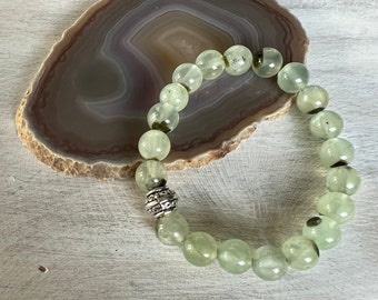 May include: A green gemstone bracelet with a silver bead charm. The bracelet is made of round, smooth beads and is strung on a stretchy cord.