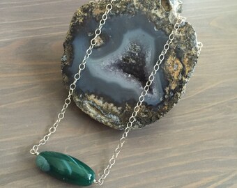 May include: A silver chain necklace with a green agate pendant. The pendant is a long, oval shape with swirls of green and white.