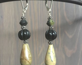 May include: A pair of dangle earrings with a teardrop-shaped green and brown stone, a black bead, and a silver bead.