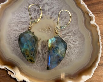 May include: A pair of gold earrings with labradorite stones. The stones are a dark blue-green color with iridescent flashes of color.