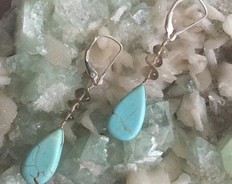 May include: A pair of dangle earrings with turquoise and smoky quartz stones. The earrings have silver leverback closures.
