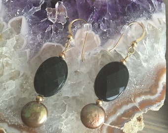 May include: A pair of gold dangle earrings with black oval shaped stones and brown pearl-like beads.