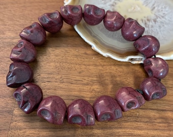 May include: A dark red skull bead bracelet with a black cord. The beads are made of stone and have a textured surface.