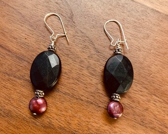 May include: A pair of dangle earrings with black oval-shaped gemstone beads and a single dark purple pearl bead on each earring.