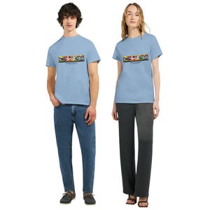May include: Two people wearing light blue t-shirts with a colorful graphic design across the chest. The shirts have short sleeves and a crew neck. The graphic includes text and various colors. One person is wearing blue jeans, and the other is wearing dark gray pants.