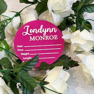 May include: Pink round acrylic birth announcement plaque with the name "Londynn Monroe" and spaces to fill in the date, time, weight, and length.