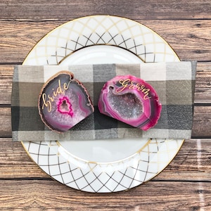 May include: Two pink agate slices with gold calligraphy, one reading "bride" and the other "groom", on a black and white checkered napkin.