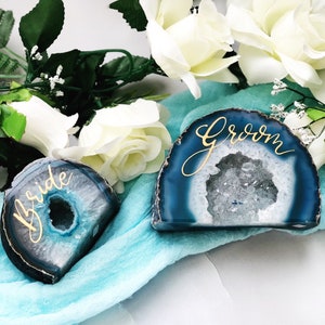May include: Two agate slices with a blue and white crystal pattern. The slices are decorated with gold calligraphy that reads "bride" and "groom".