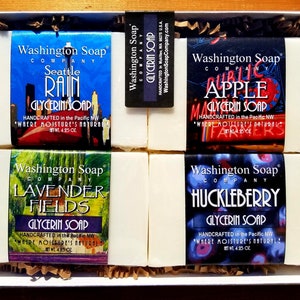 May include: A white gift box filled with four bars of glycerin soap. The soaps are labeled with the Washington Soap Company logo and the scents: Seattle Rain, Public Apple, Lavender Fields, and Huckleberry. Each bar is 4.25 oz.