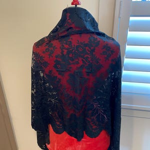 May include: Black lace shawl with a floral pattern. The shawl is draped over a red dress form.