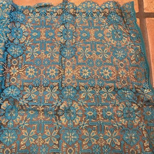 May include: Teal and gold lace fabric with a geometric pattern. The fabric has a delicate, intricate design.
