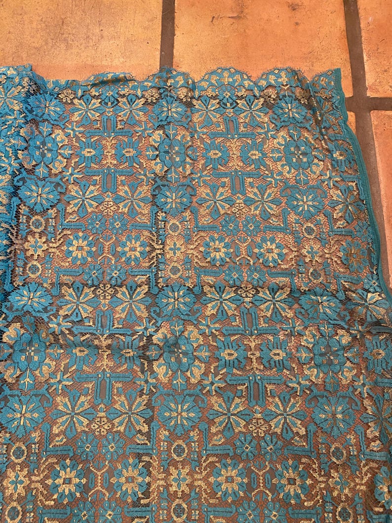 May include: Teal and gold lace fabric with a geometric pattern. The fabric has a delicate, intricate design.