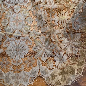 May include: A close-up of a gold and white lace fabric with a floral pattern. The lace is delicate and intricate, with a slightly textured surface.
