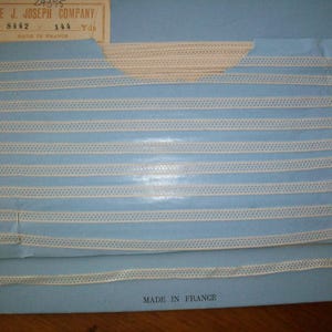 May include: A white, decorative trim with a delicate, openwork design. The trim is displayed on a blue background with the text "THE J. JOSEPH COMPANY" and "MADE IN FRANCE".